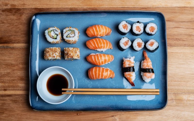 sushi-plate-with-maki-uramaki-nigiri-california-roll-blue-plate-soy-chopsticks-asian-gastronomic-food-composition-wooden-background sushi-plate-with-maki-uramaki-nigiri-california-roll-blue-plate-soy-chopsticks-asian-gastronomic-food-composition-wooden-background